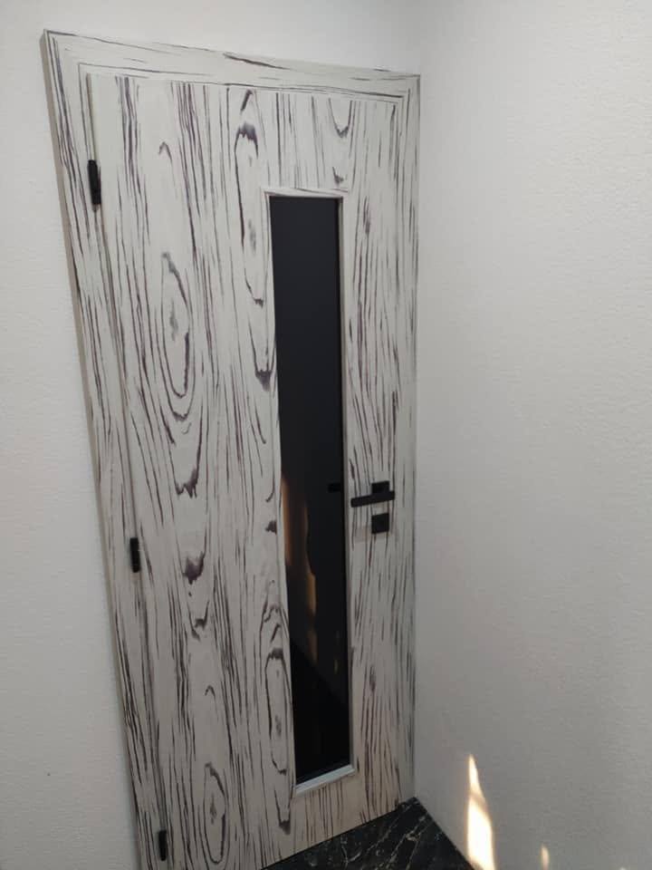 Einzelne Tür mit schwarz-weißer Holzmaserung und schmalem Glas
