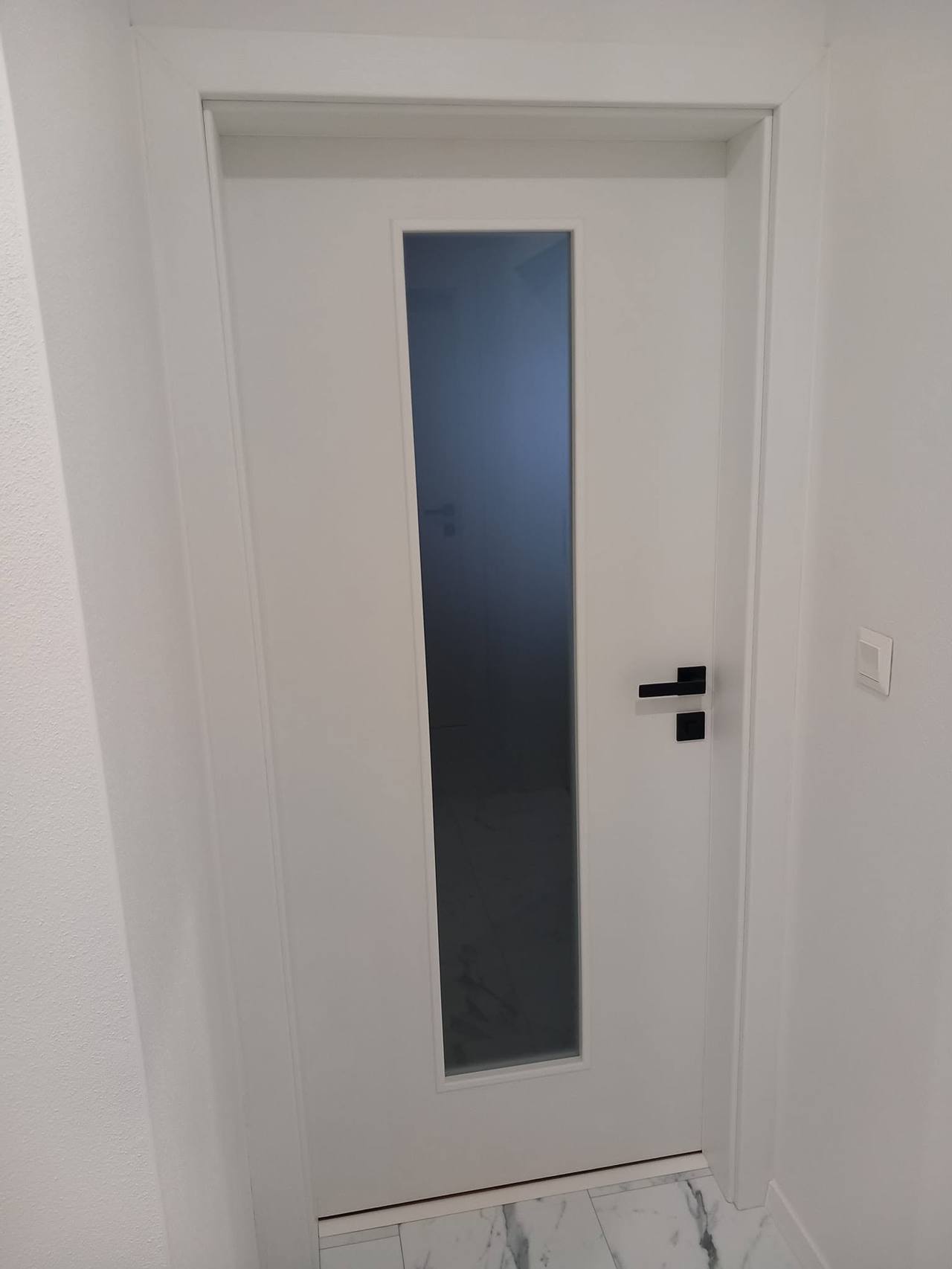 Weiße Tür mit dunklem senkrechtem Glas und schwarzer Klinke