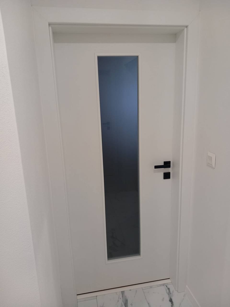 Weiße Tür mit dunklem senkrechtem Glas und schwarzer Klinke