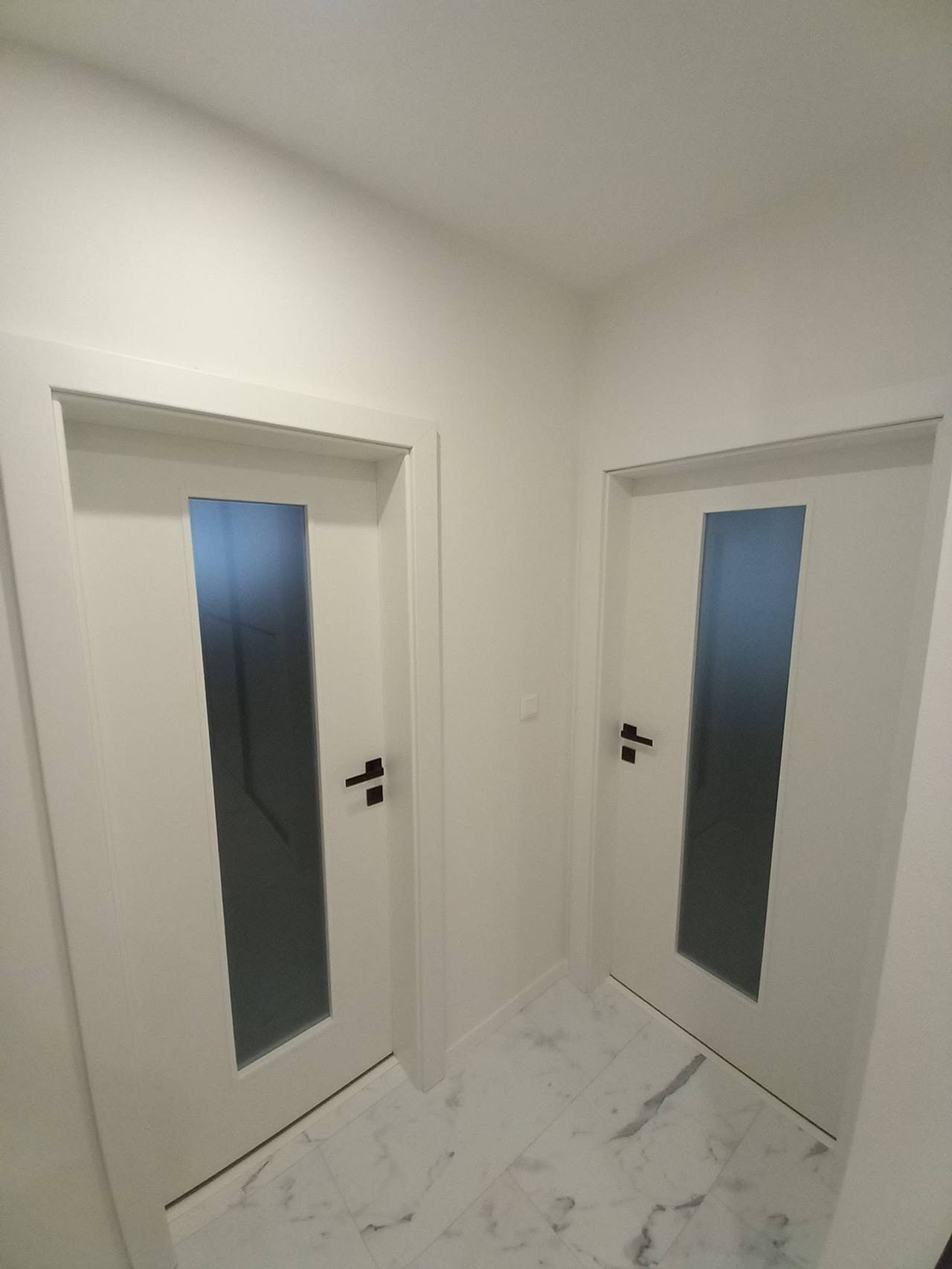Zwei weiße Türen mit dunklem Glas auf beiden Flurseiten