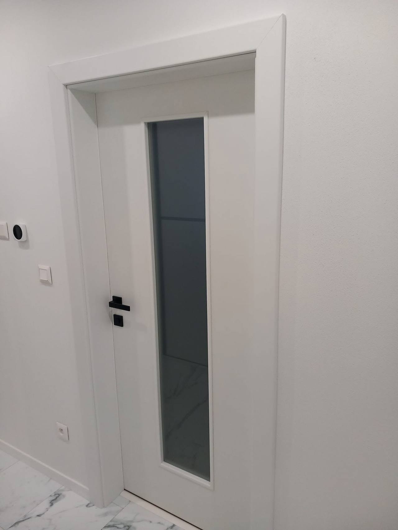 Detail der weißen Tür mit dunklem senkrechtem Glas und schwarzem Beschlag