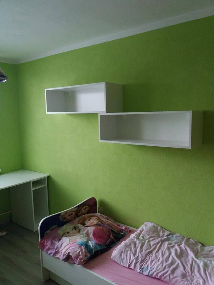 Dve posunuté biele police nad posteľou v detskej izbe
