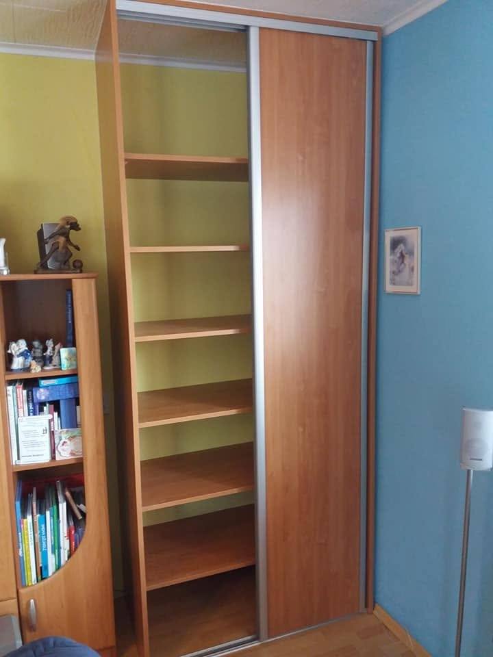Kleiderkasten in Kirschbaum-Dekor mit angelehnter Tür neben dem Regal.