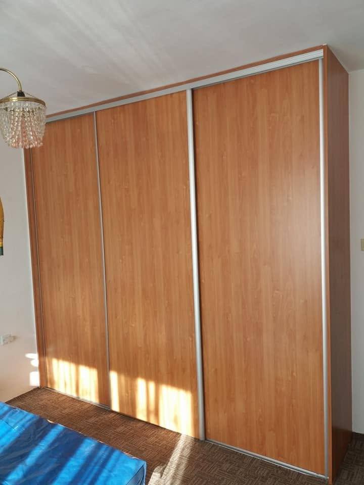 Dreitüriger Kleiderkasten in Kirschbaum-Dekor im hellen Zimmer mit Kronleuchter.