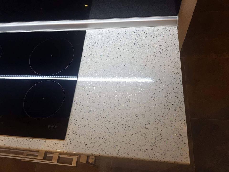 Induktionsfeld und helle Terrazzoplatte mit LED-Streifen über schwarzem Glas.