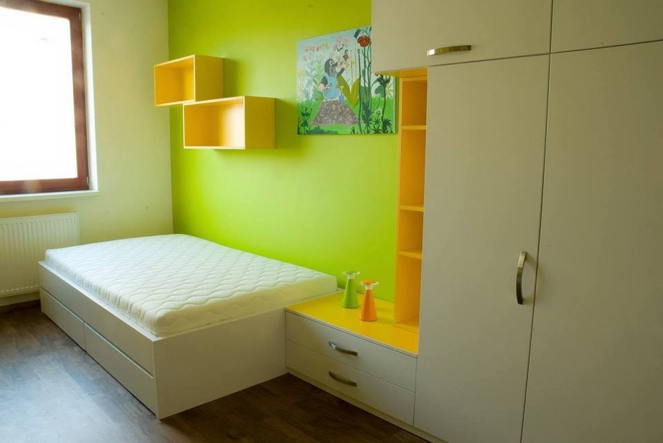 Kinderzimmer mit weißem Bett, gelben Fachböden und Kleiderkasten