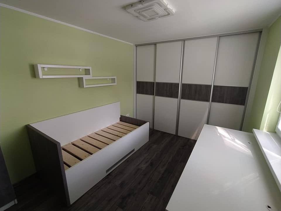 Niedriges Bett vor der grünen Wand neben dem Schwebetürenkasten