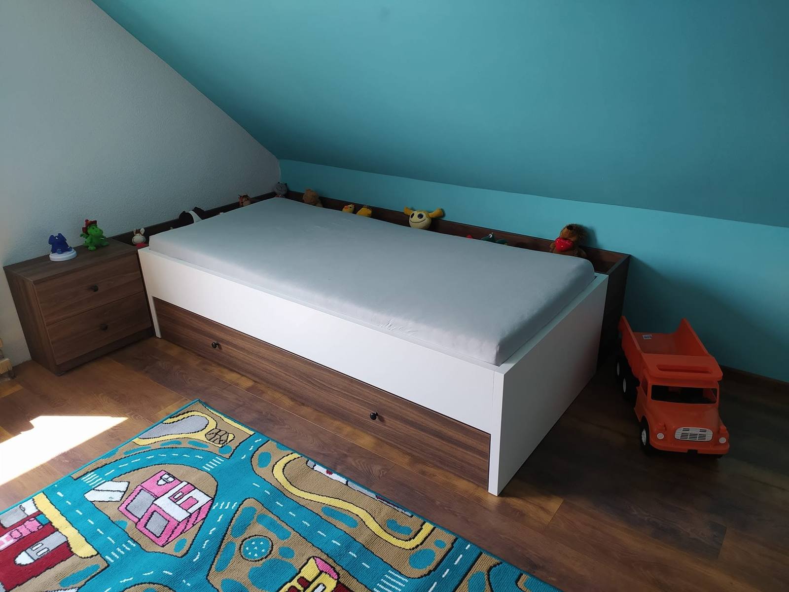 Posteľ pod šikminou s tmavým soklom a hračkami