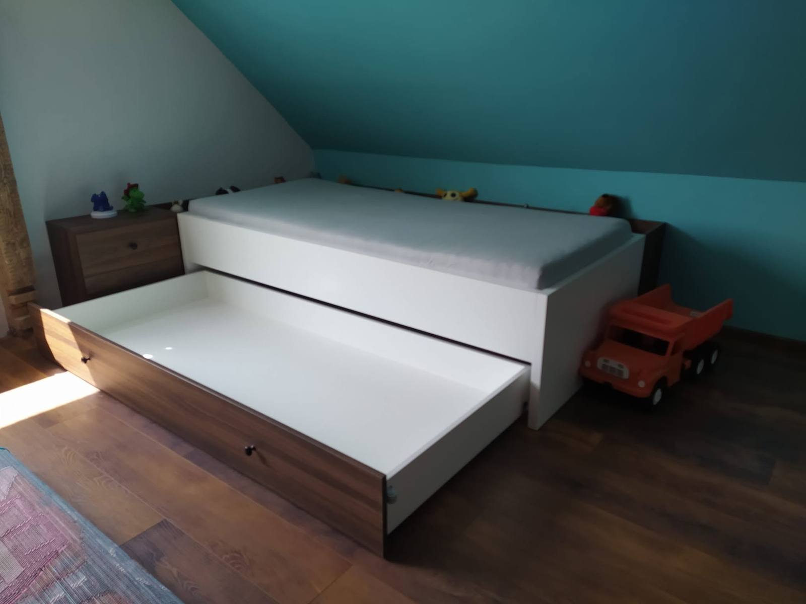Vysunutá prístelka pod bielou posteľou v podkroví
