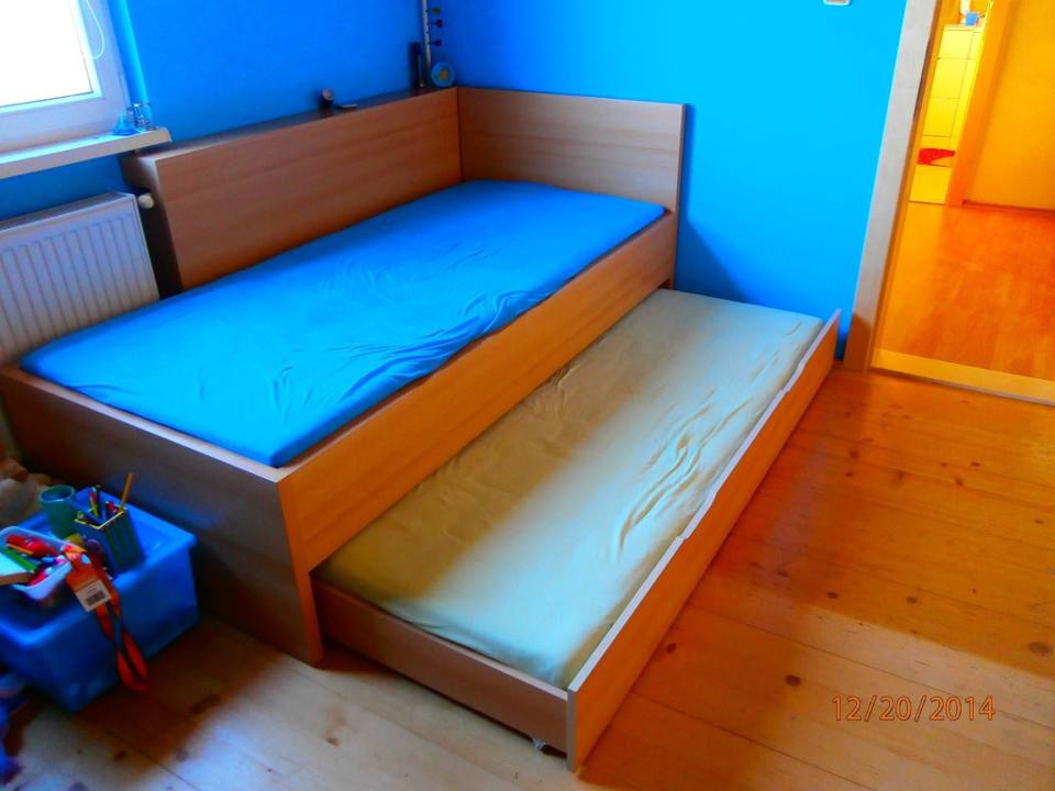 Kinderbett mit ausgezogener Zusatzliege vor blauer Wand