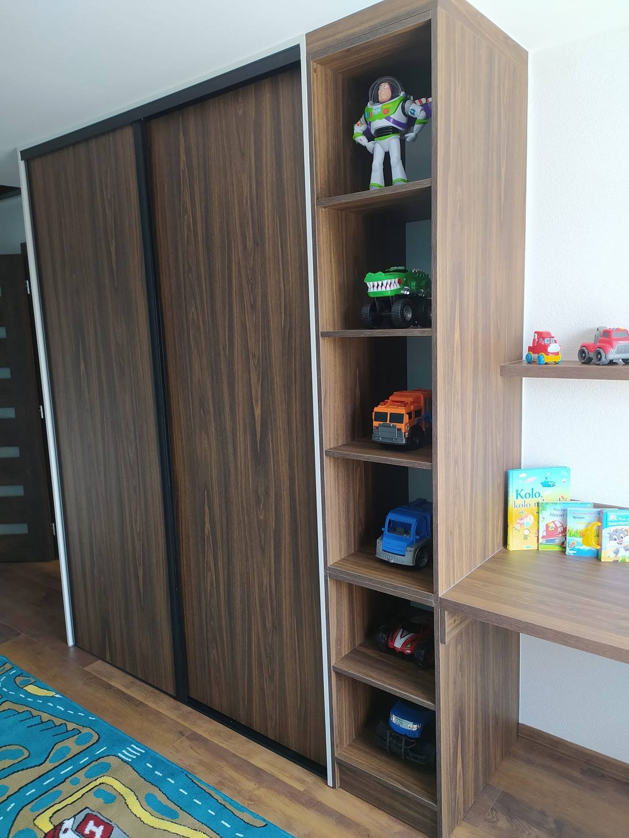Kinderzimmerkasten mit dunklen Schiebetüren und einer Säule offener Fächer mit Spielsachen.