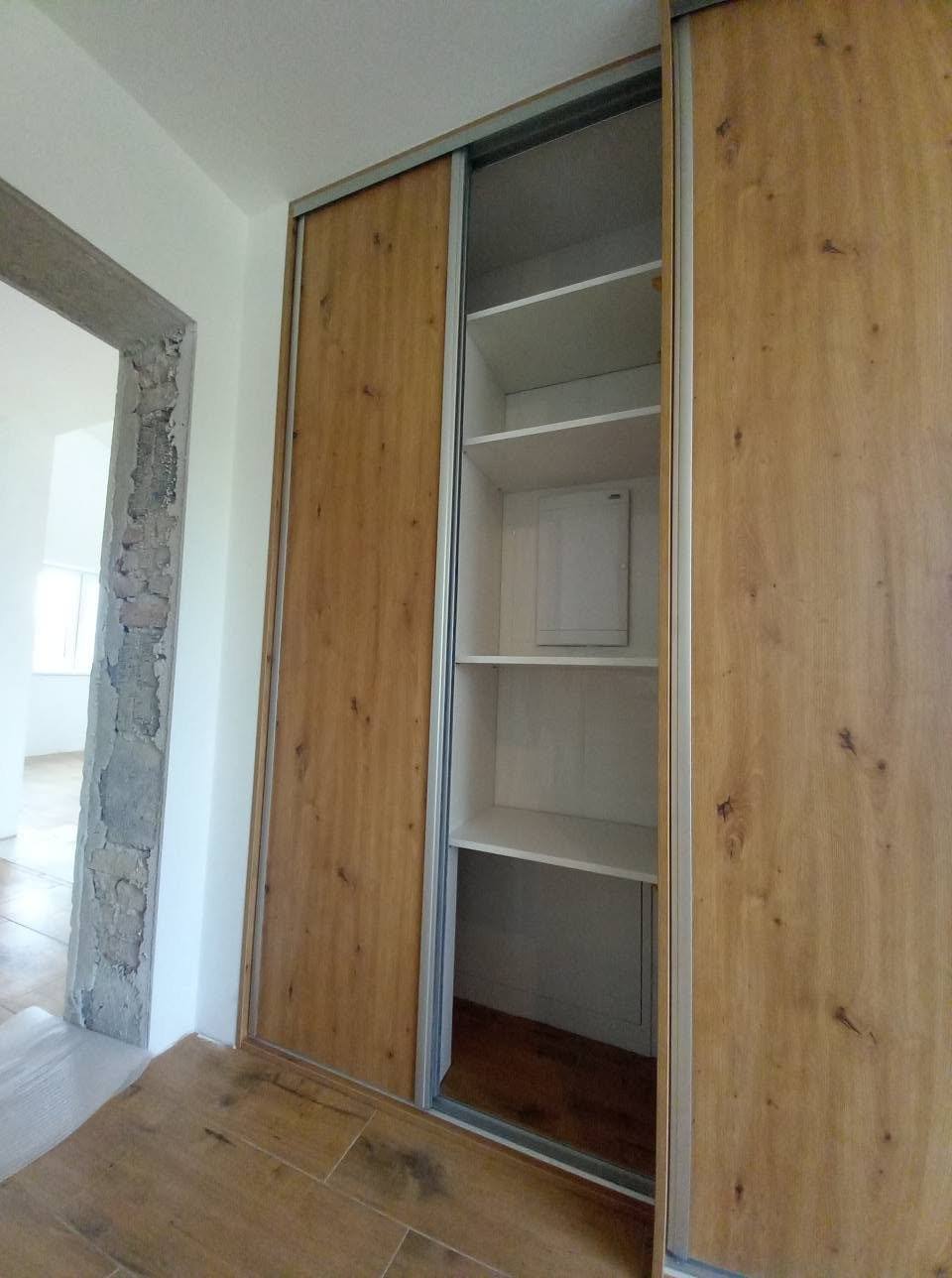 Schiebetürkasten in Eichendekor mit offenem, weißem Innenraum.