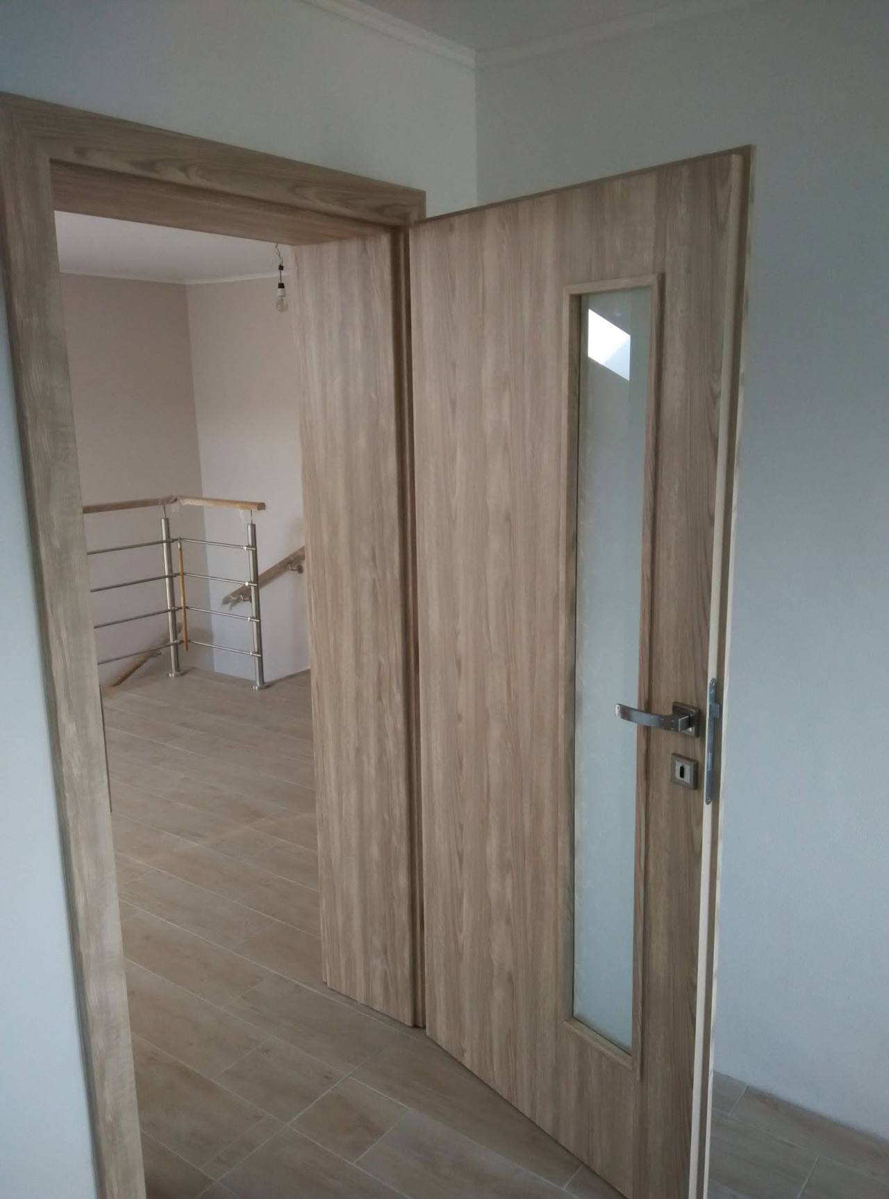 Eichentür mit schmalem Glasstreifen neben dem Metallgeländer der Stiege