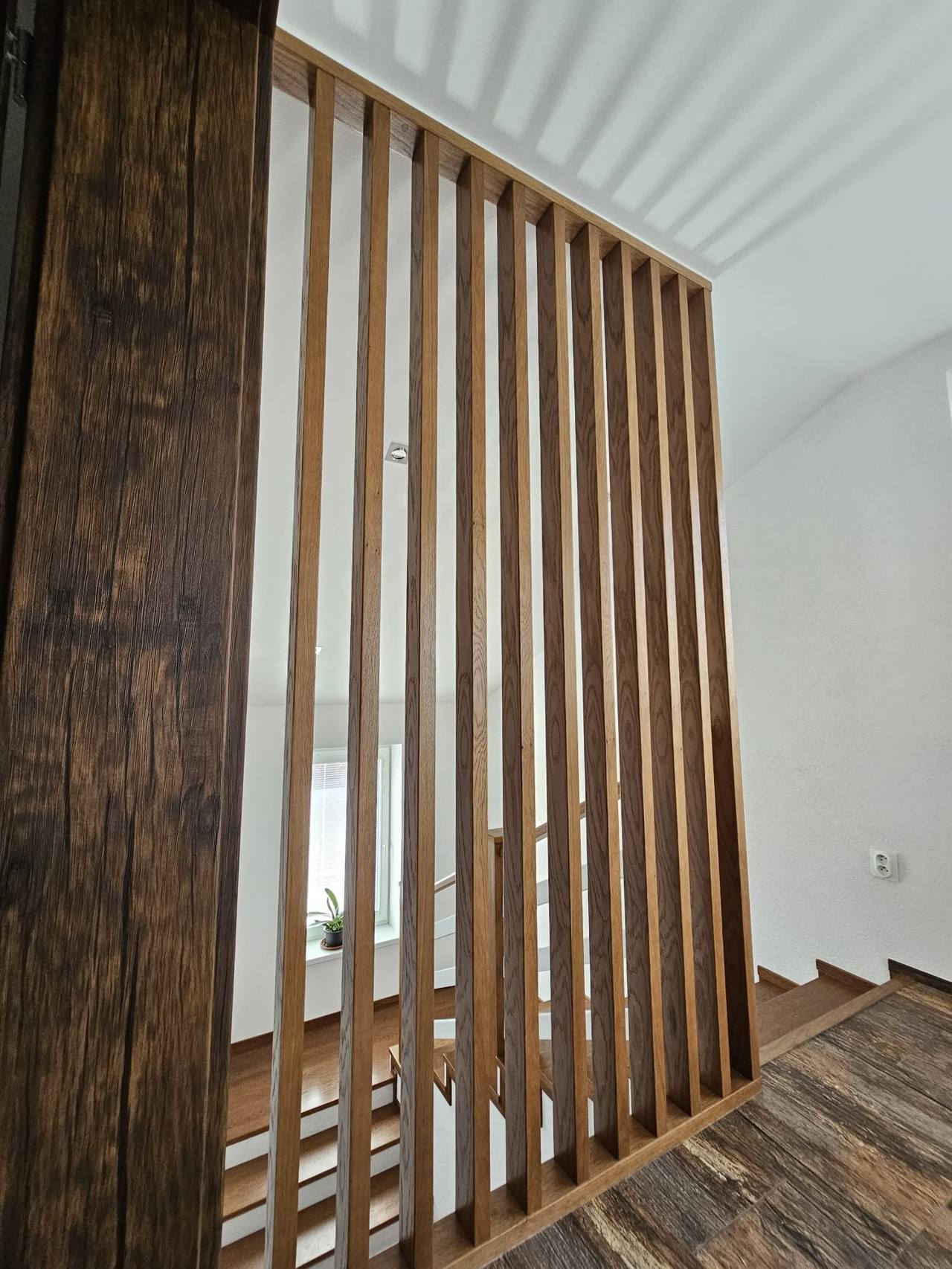 Senkrechte Eichenlamellen des Geländers neben altem Holzbalken