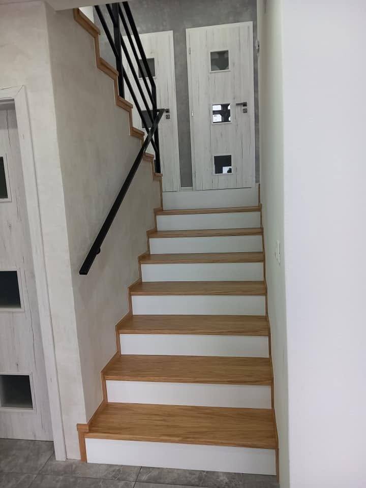 Gerade Stiege mit Eichenstufen und schwarzem Handlauf an der Wand
