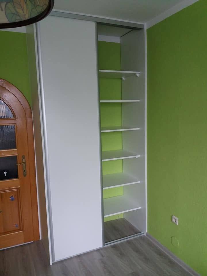 Jedna zo skríň otvorená, s bielymi policami pri zelenej stene