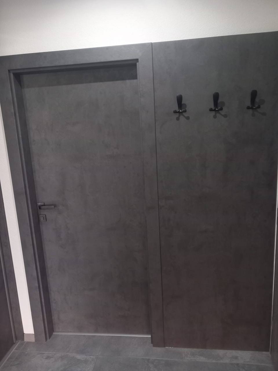 Tür in dunklem Betondekor bündig in der Wand neben den Garderobenhaken