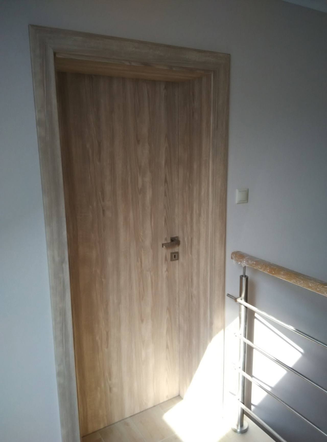 Massive Tür in Eichendekor bei der Stiege mit Edelstahlgeländer.