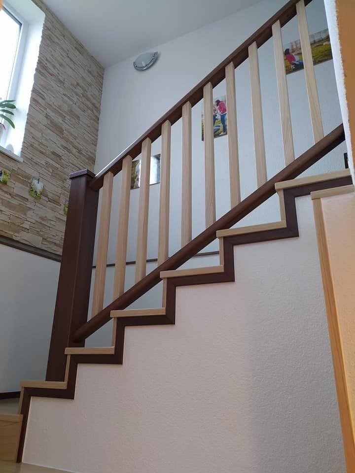 Zweifarbiges Geländer mit hellen Stäben neben der Steinwand