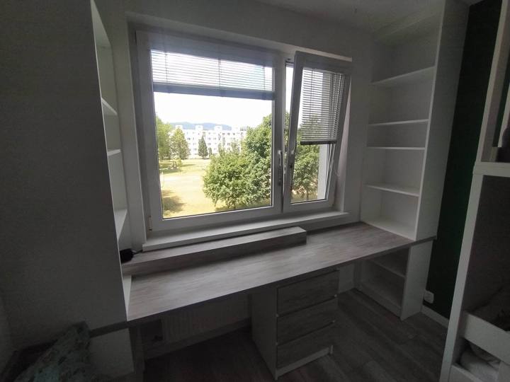 Schreibtisch unter dem Fenster gesäumt von offenen Regalen