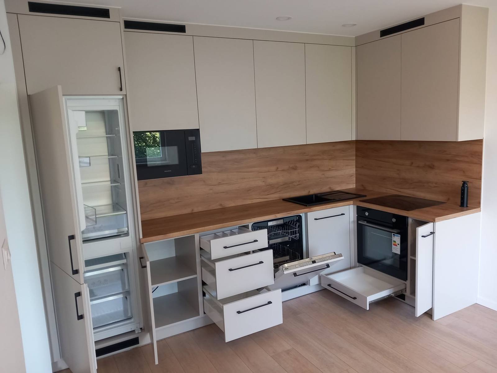 Kaschmirfarbene L-Küche mit geöffnetem Kühlschrank, Laden und Backrohr