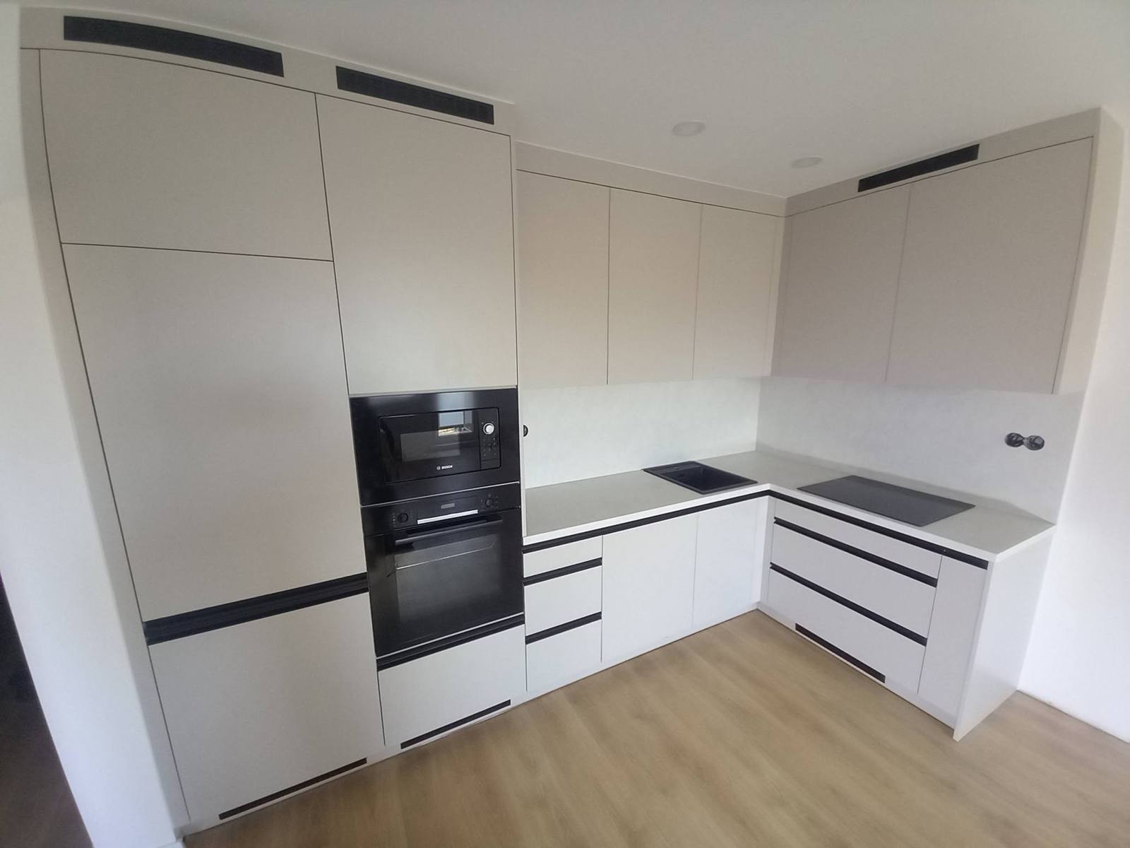 Helle Eckküche mit Hochschrank und schwarzem Backrohr.