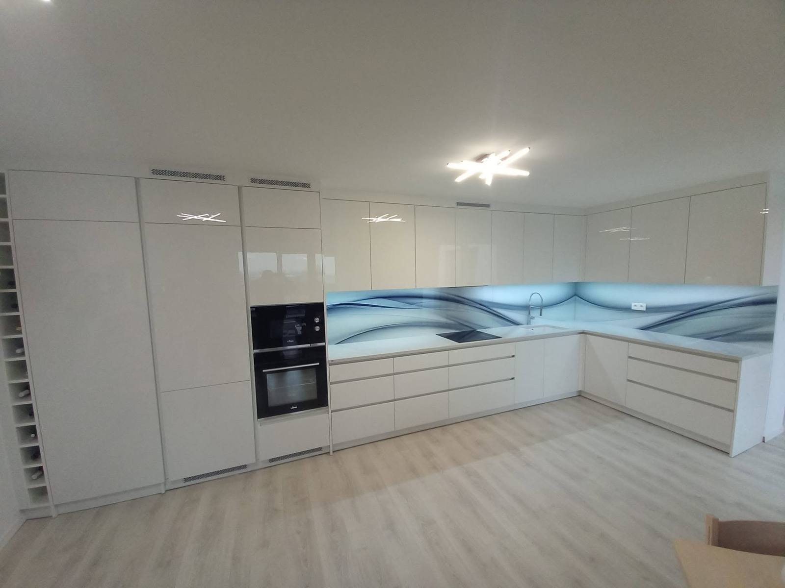 Hochschrank mit Einbaubackrohr neben der Glaswand mit blauem Motiv.