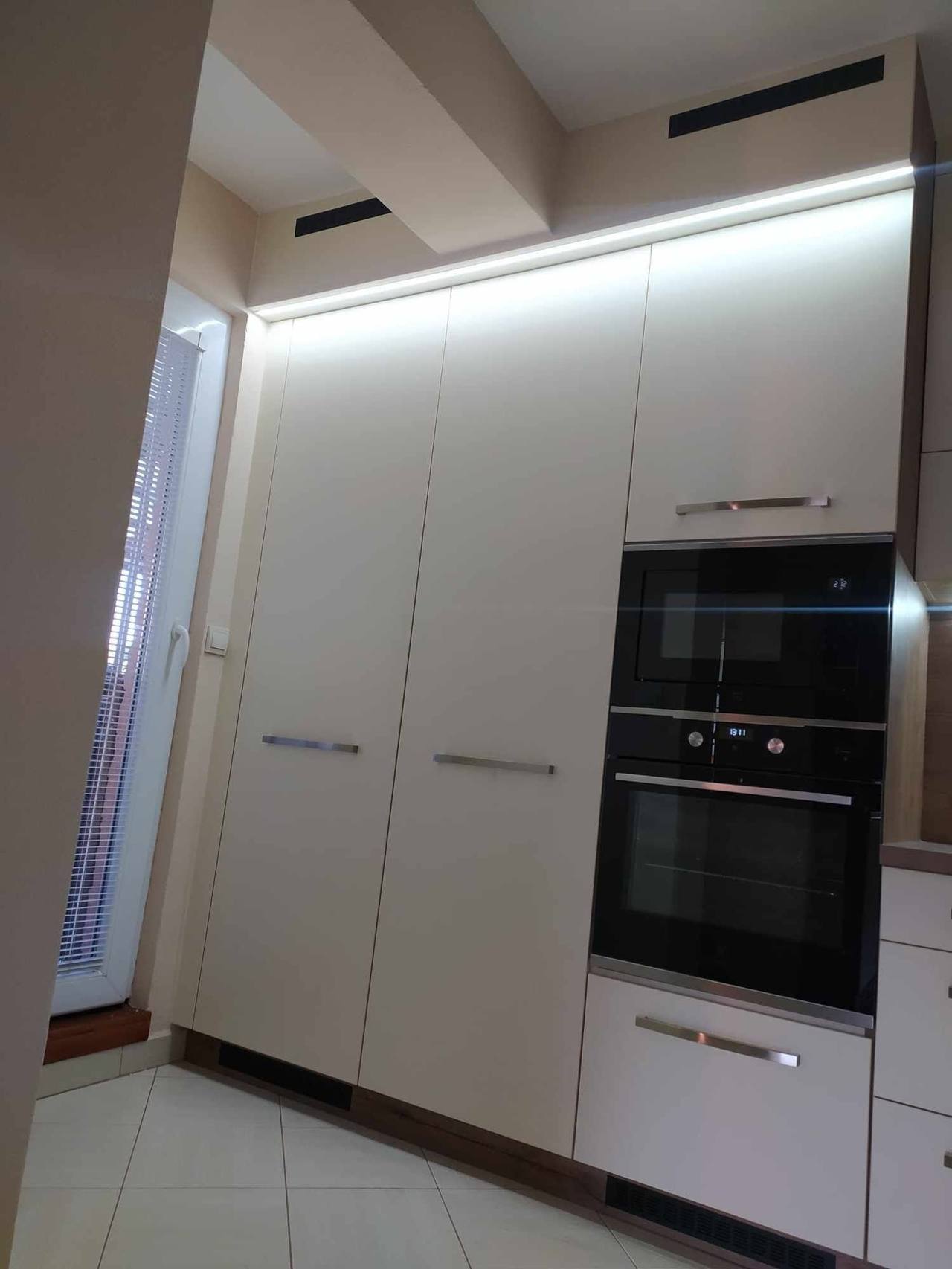 Wand aus cremefarbenen Hochkästen mit Einbaugeräten und LED-Licht