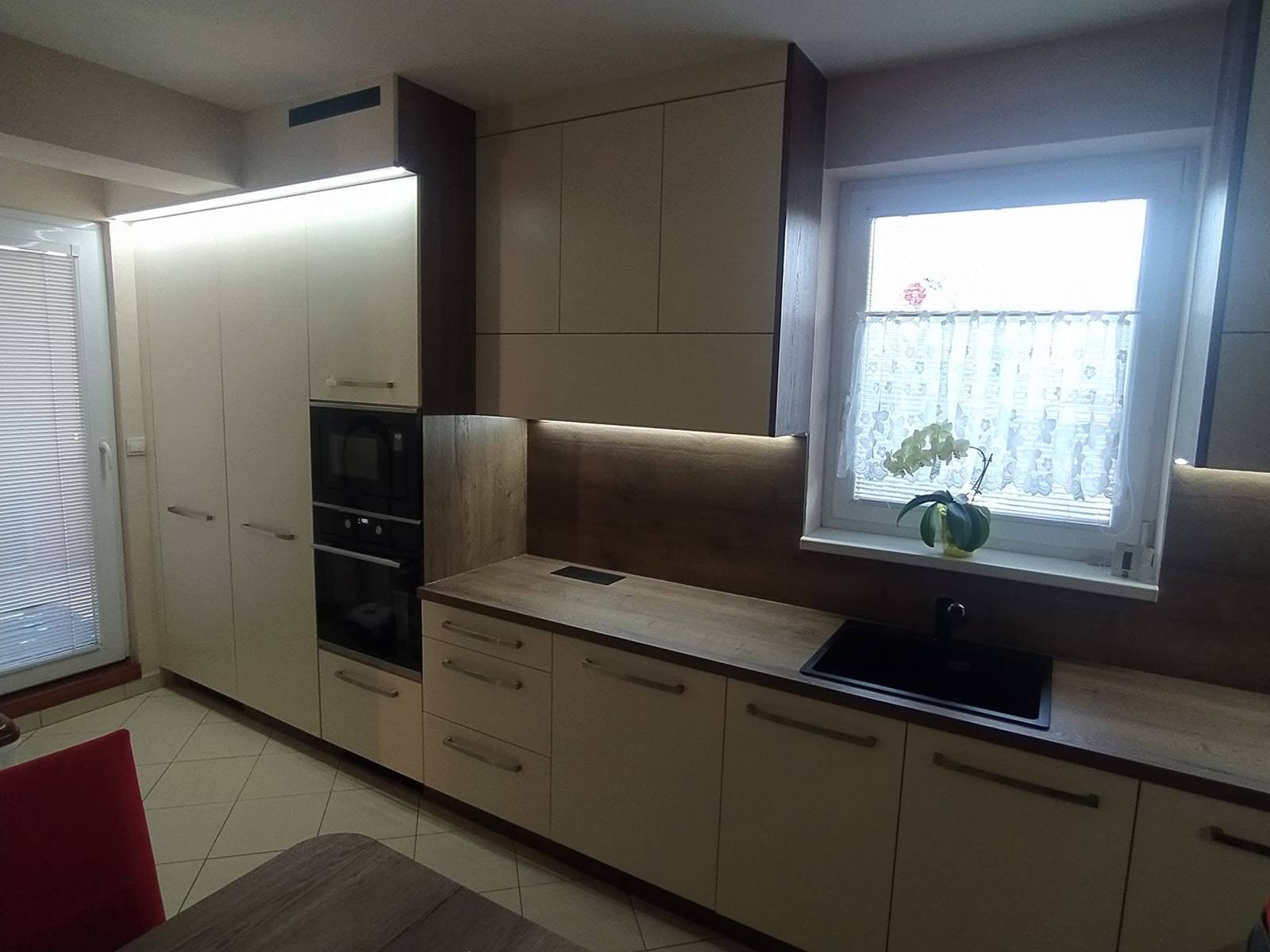 Cremefarbene Zeile mit Spüle unter dem Fenster und beleuchteter Rückwand