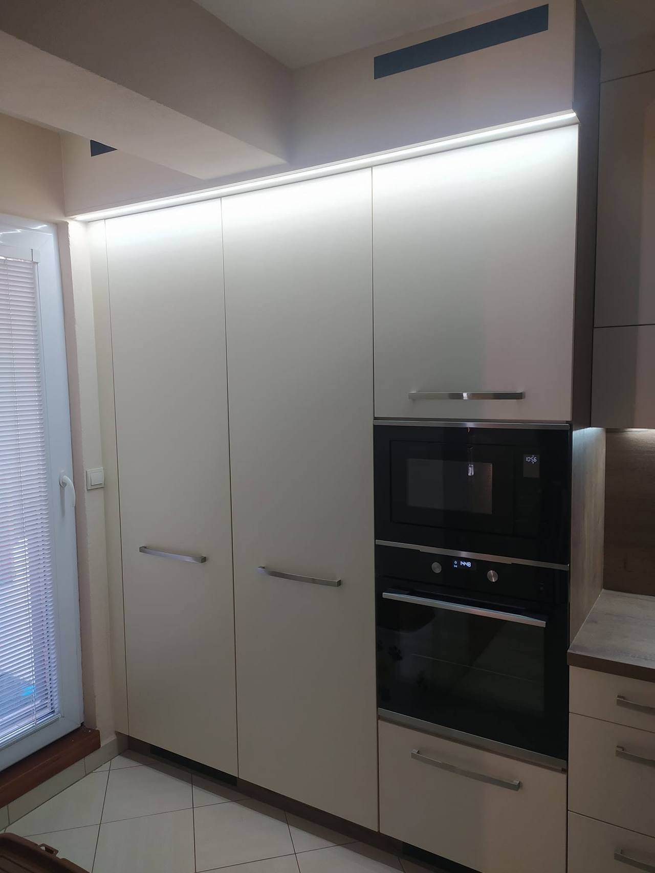 Cremefarbene Hochkästen mit Backrohr und Mikrowelle unter LED-Band