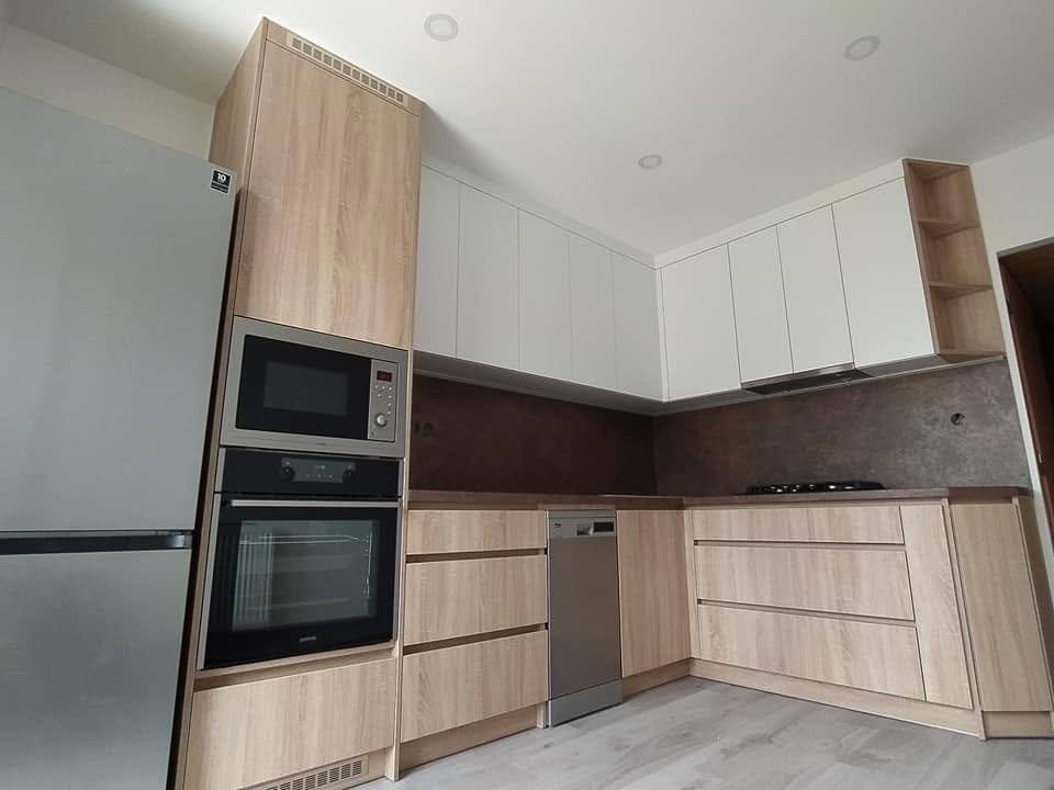 Edelstahl-Kühlschrank neben Eichenhochkasten und braune Rückwand
