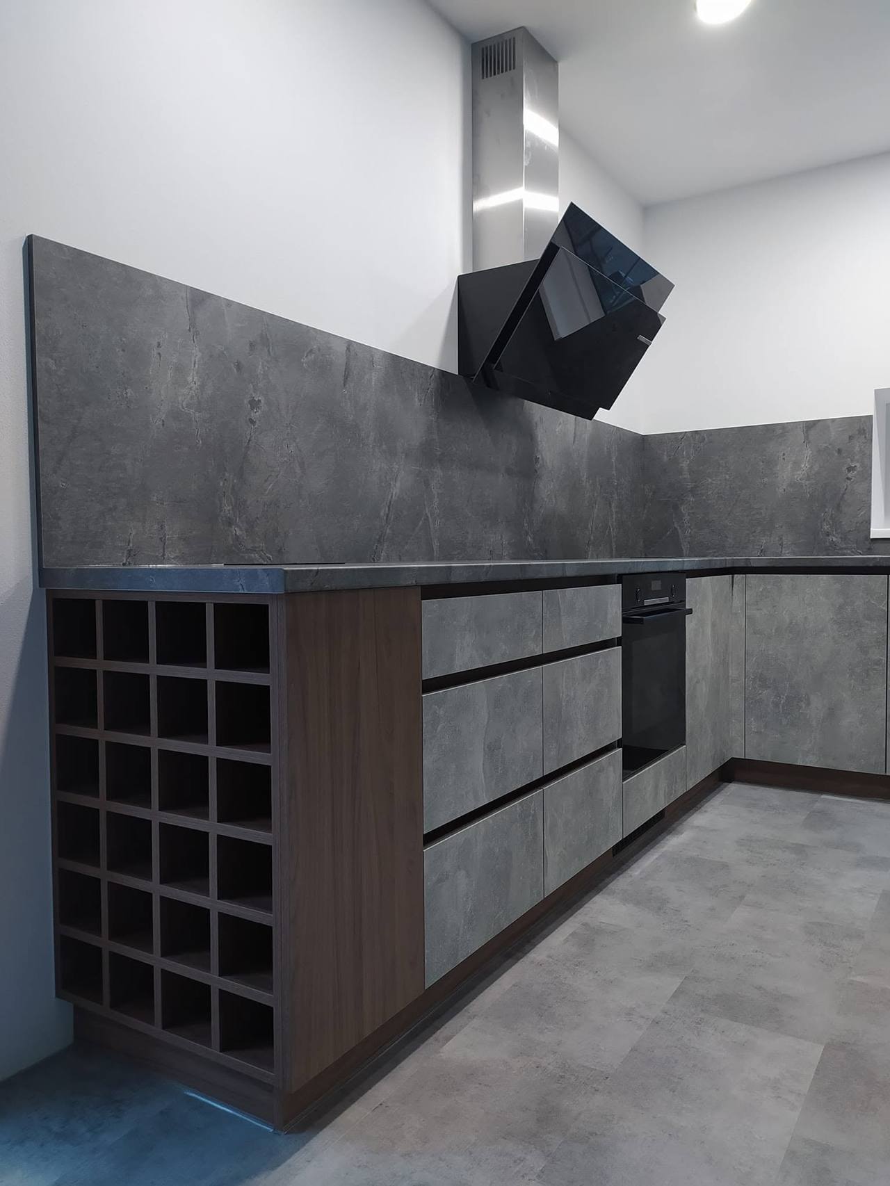 L-Küche mit Rückwand in Betonoptik und schrägem Dunstabzug