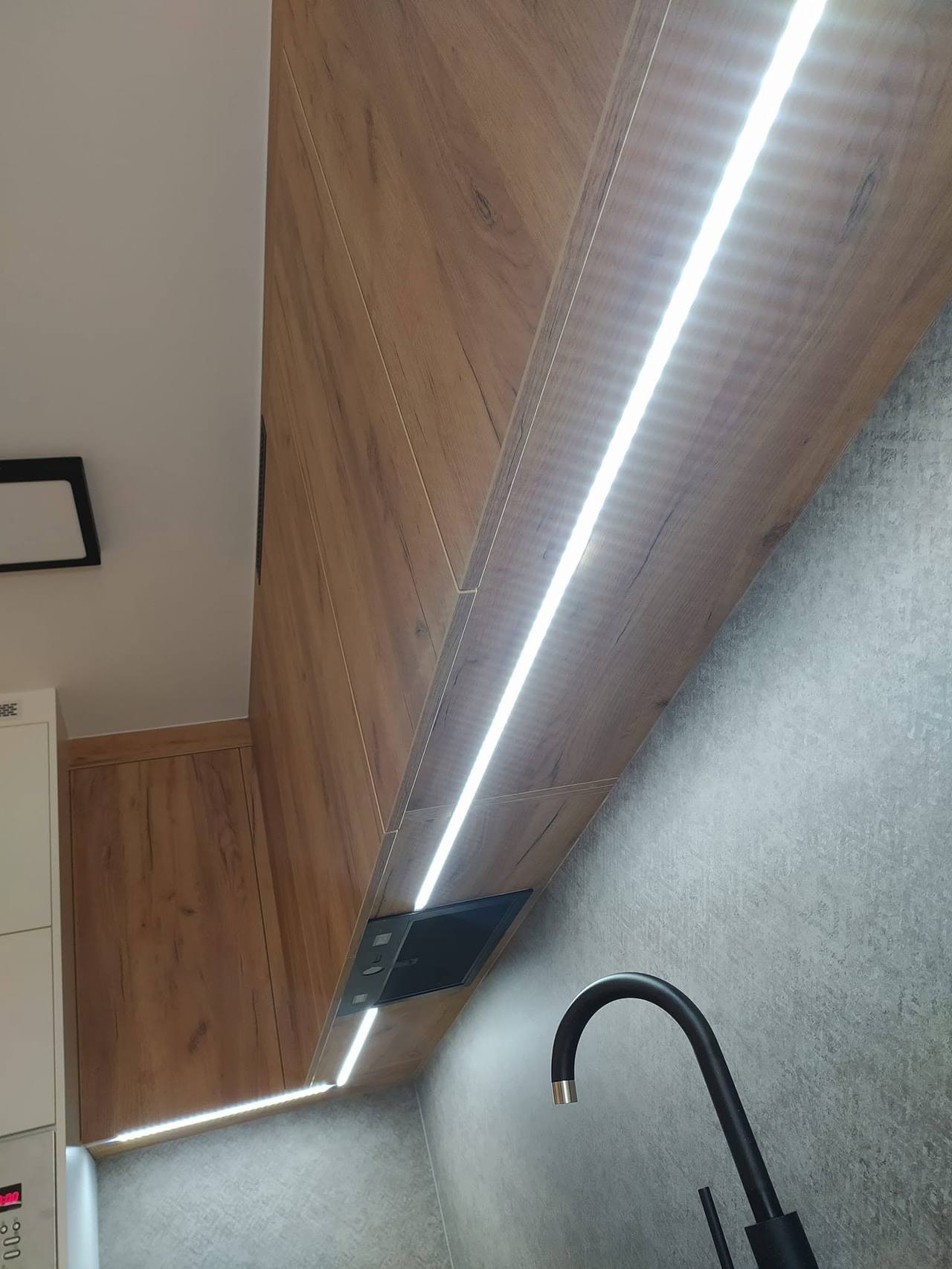 LED-Leiste unter Oberkasten in Holzdekor über schwarzer Armatur