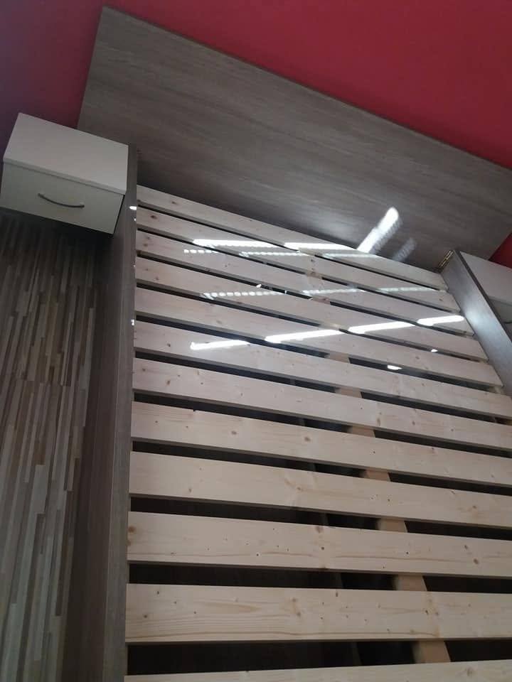 Manželská posteľ so sivým čelom a stolíkom pri bordovej stene