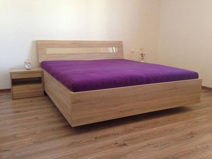Doppelbett in Eichendekor mit violetter Tagesdecke und Nachtkästchen