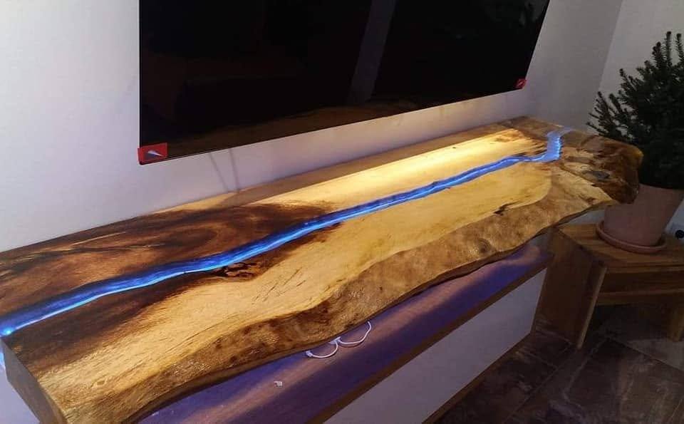 Hinterleuchtetes Massivholzbord mit blauem Harz unter dem Fernseher