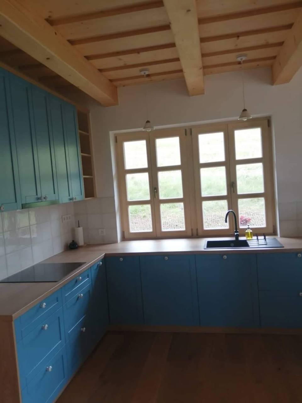 Blick auf die blaue Eckküche unter der Holzbalkendecke