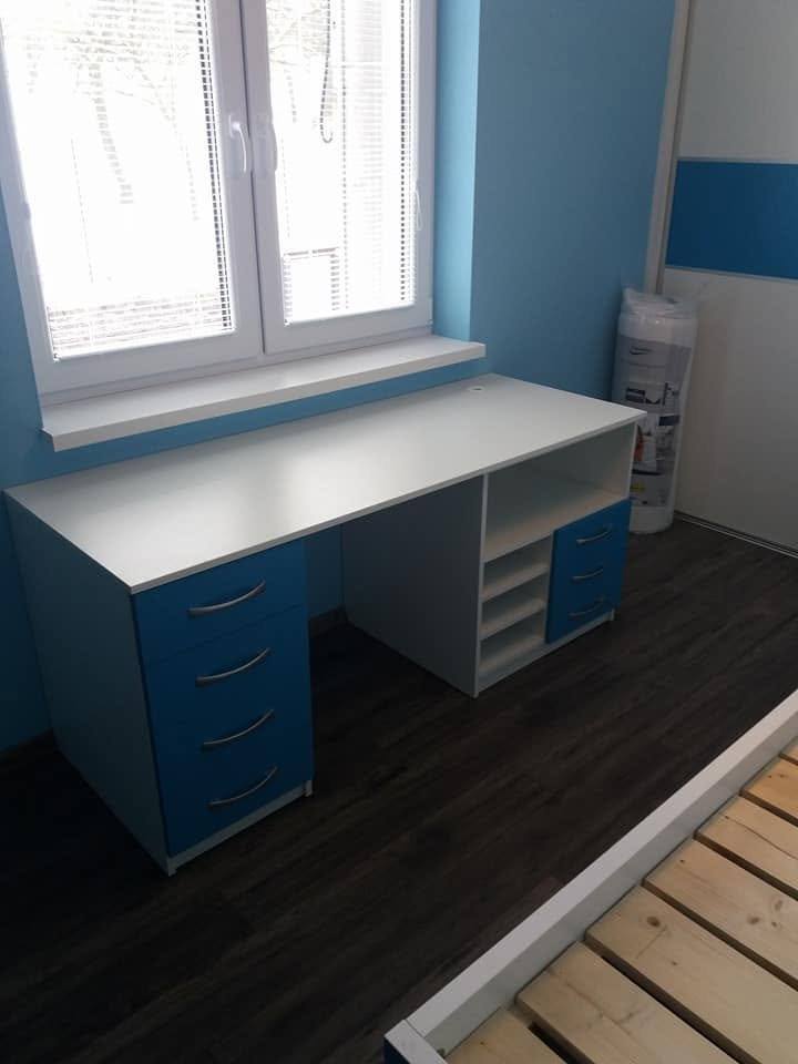 Písací stôl s modrými zásuvkami pod oknom