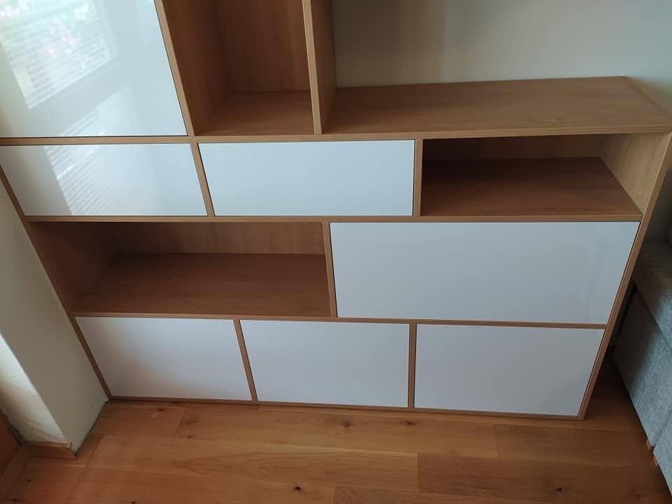 Detail spodnej časti steny s bielymi dvierkami a dubovými priehradkami