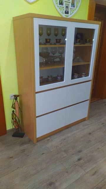 Vitrine in hellem Holzdekor mit weißen Rahmen vor grüner Wand