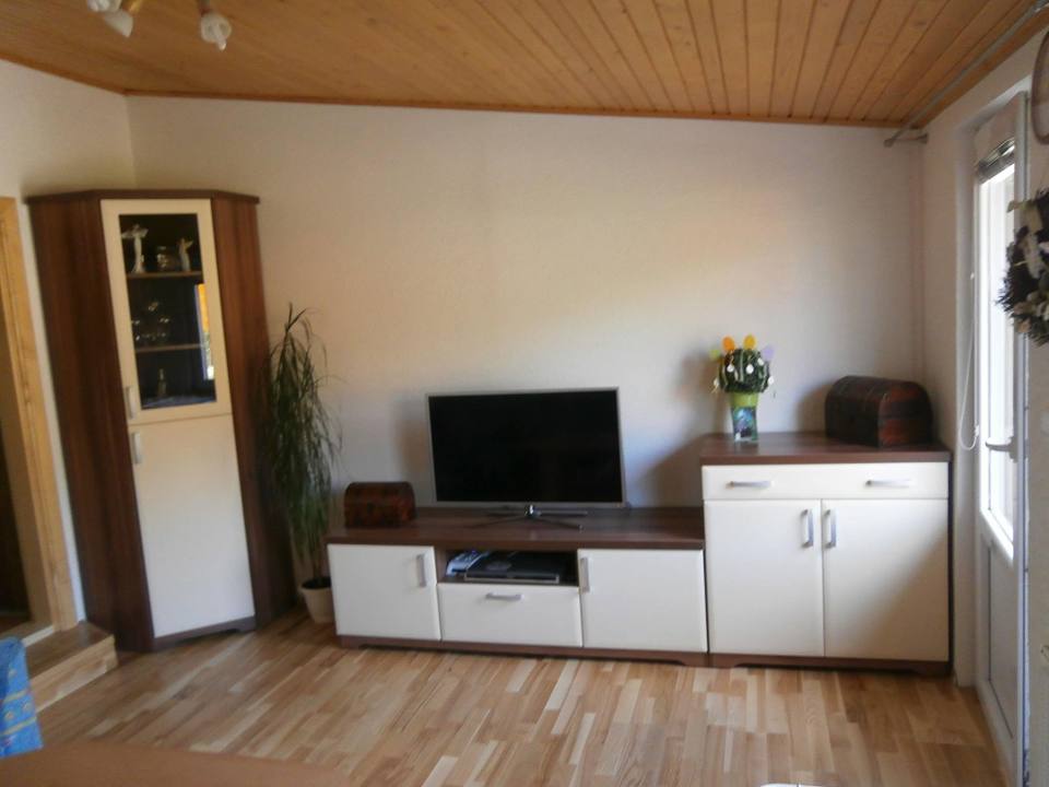 Wohnzimmer mit Eckvitrine, TV-Lowboard und Kommode unter der Holzdecke