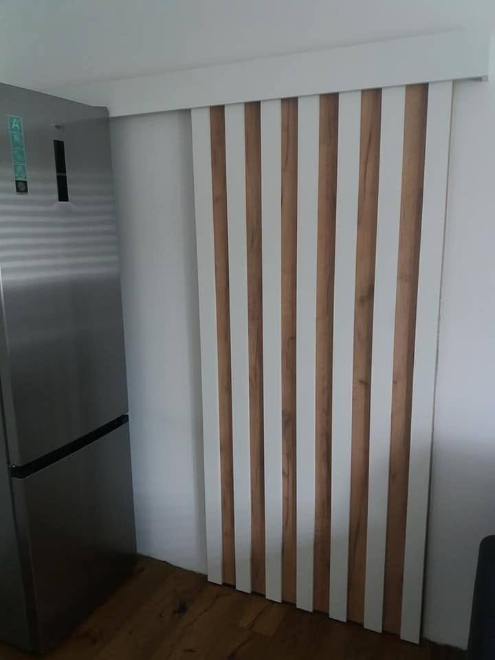 Vertikale Eichenlamellen an weißer Wand neben Edelstahlkühlschrank