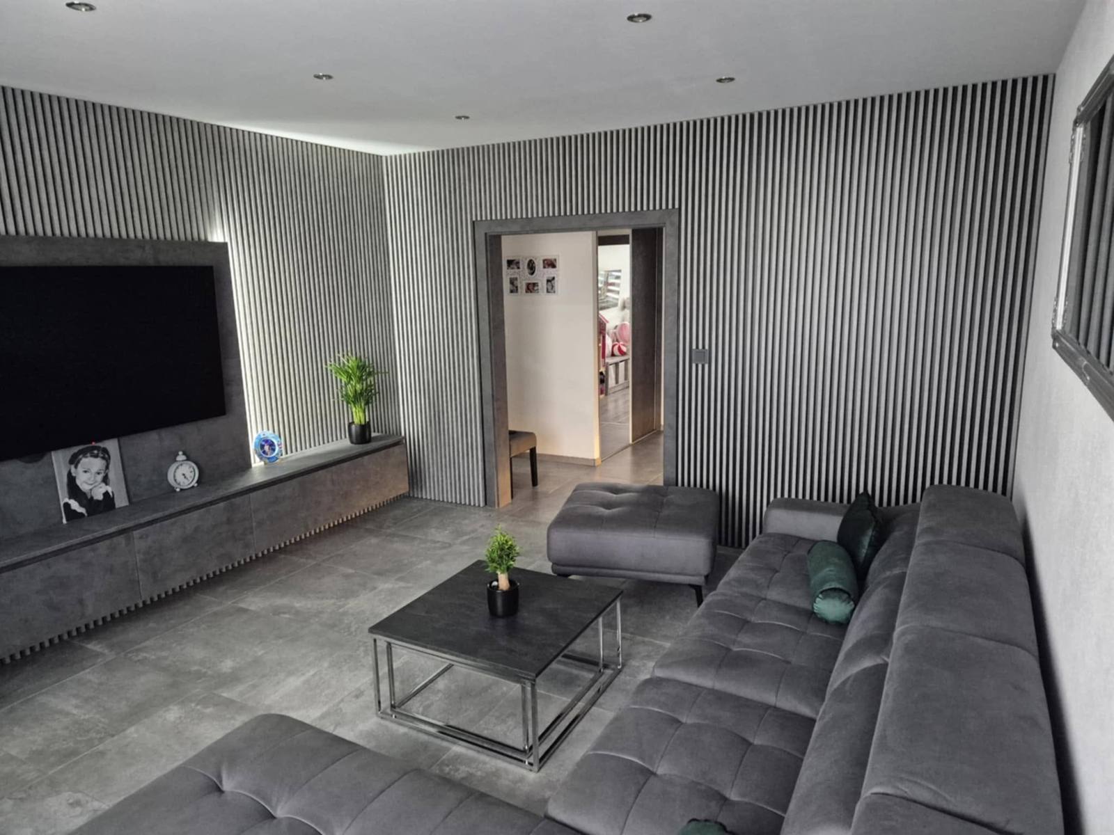 Wohnzimmer mit grauer Lamellenwand, TV-Hängeelement und Ecksofa