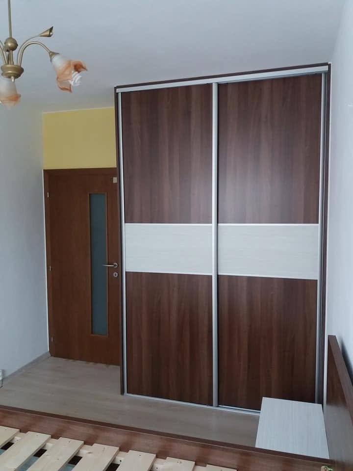 Kleiderkasten in Nussbaum-Dekor mit cremefarbenem Band in der Mitte.
