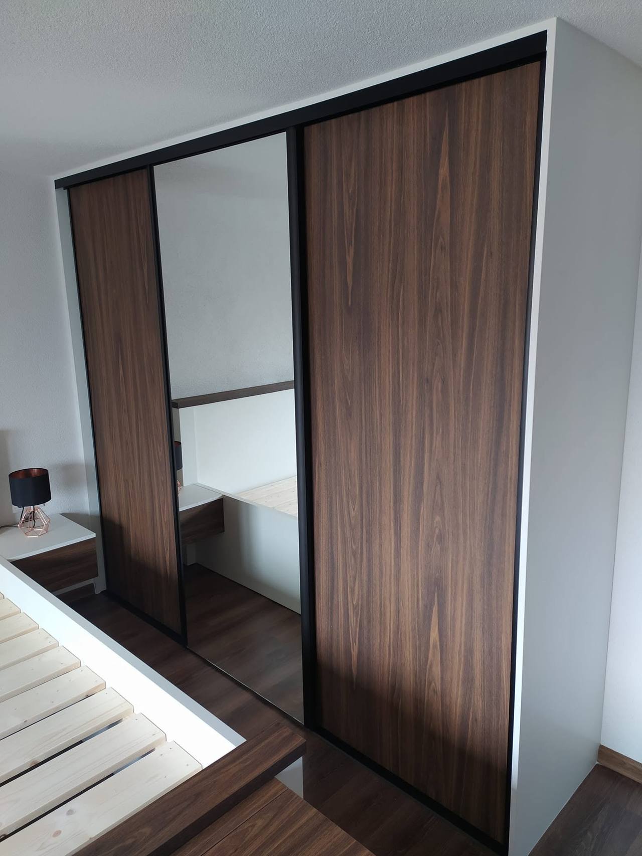 Kleiderkasten in Nussbaum-Dekor mit Spiegel und schwarzen Profilen im Schlafzimmer.