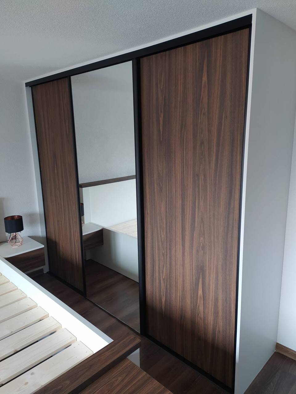 Kleiderkasten in Nussbaum-Dekor mit Spiegel und schwarzen Profilen im Schlafzimmer.