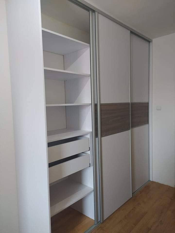 Otvorená biela posuvná skriňa s orechovým pásom a zásuvkami.