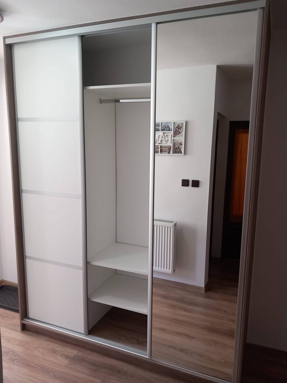 Otvorená biela skriňa s deleným čelom, zrkadlom a tyčou