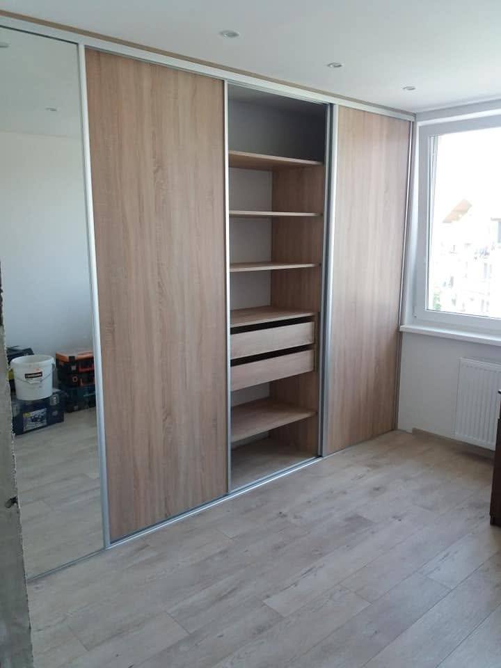 Geöffneter Schiebetürkasten in Eichendekor mit Fachböden und Laden am Fenster.