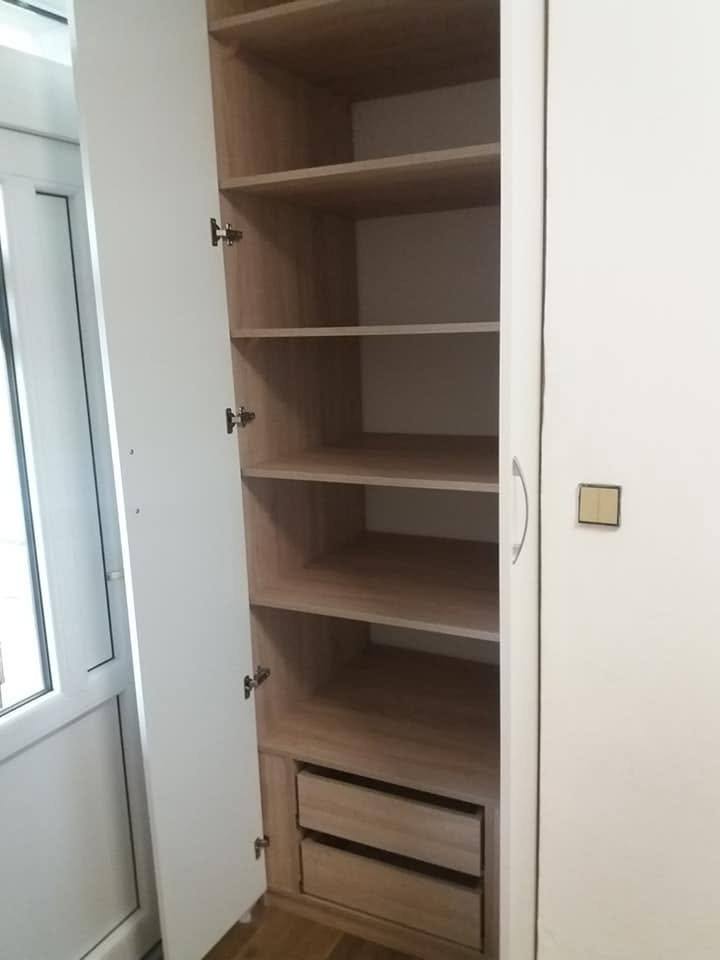 Offener Kasten in Eichendekor mit Fachböden und dunkler Lade am Fenster.